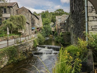 A small river flowing through a village with stone buildings and greenery at Rose Cottage in Ambleside
