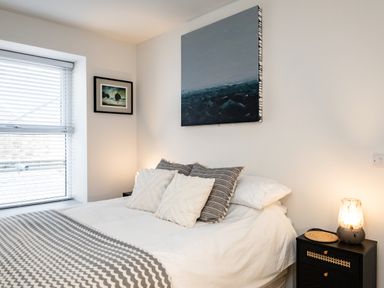 A bedroom with a bed with pillows and a blanket a bedside table with a lamp and two paintings on the wall at The Lookout in Polzeath