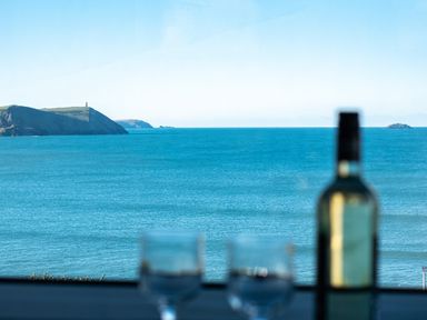 A view of the ocean with distant hills and a bottle and two glasses in the foreground at The Lookout in Polzeath