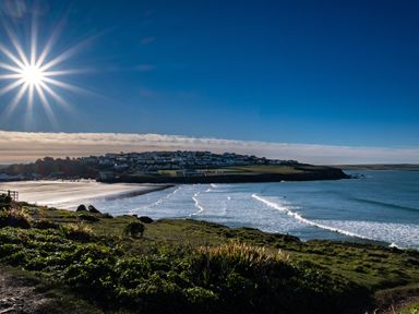 A coastal view with waves hitting the shore and houses on a hill under a bright sun at The Lookout in Polzeath