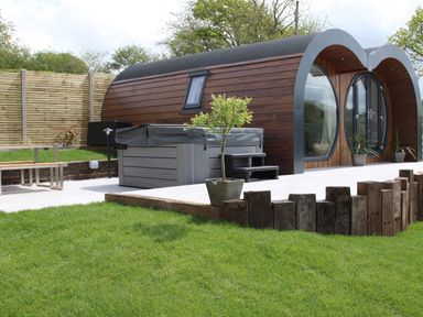 A garden with a wooden curved cabin a hot tub potted plants and wooden fencing at Creuddyn in Llanfihangel-y-Creuddyn near Aberystwyth