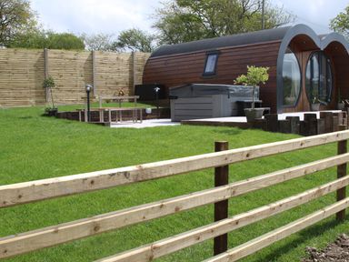 A fenced grassy yard with a modern wooden pod cabin hot tub and outdoor seating at Creuddyn in Llanfihangel-y-Creuddyn near Aberystwyth
