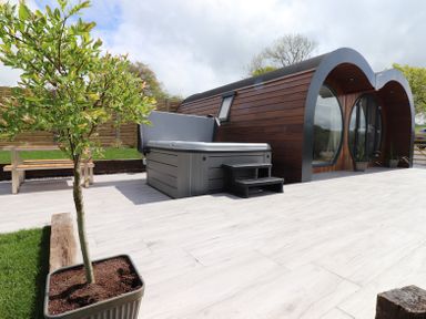 An outdoor area with a wooden pod cabin featuring curved roof and hot tub on a tiled patio at Creuddyn Llanfihangel-y-Creuddyn near Aberystwyth