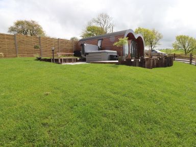 A garden with a small modern wooden cabin a hot tub a wooden fence and green grass at Creuddyn in Llanfihangel-y-Creuddyn near Aberystwyth