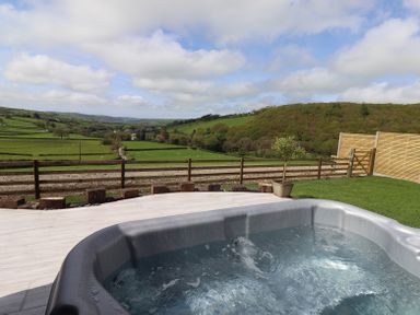A hot tub on a patio overlooking green fields and hills at Creuddyn in Llanfihangel-y-Creuddyn near Aberystwyth