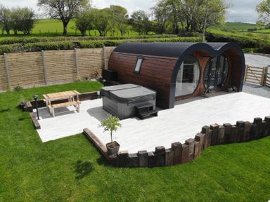 A small wooden cabin with a curved roof next to a hot tub and a picnic table on a patio surrounded by grass at Creuddyn Llanfihangel-y-Creuddyn near Aberystwyth