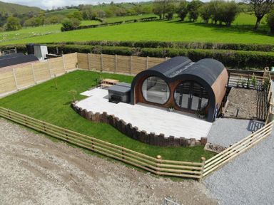 A modern pod-shaped cabin with large round windows on a patio surrounded by grass and wooden fencing at Creuddyn in Llanfihangel-y-Creuddyn near Aberystwyth