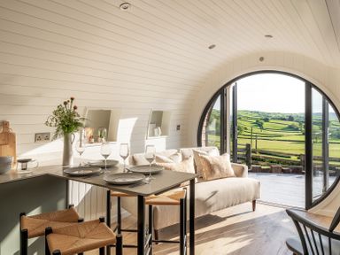 A dining area with a table set for four and a sofa near a large round window showing a countryside view at Creuddyn in Llanfihangel-y-Creuddyn near Aberystwyth