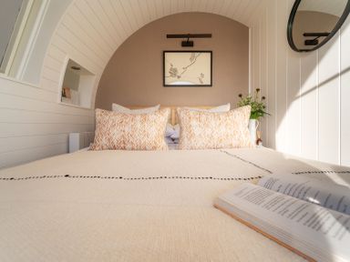 A bedroom with a bed pillows a book on the blanket a round mirror and a framed picture at Creuddyn in Llanfihangel-y-Creuddyn near Aberystwyth