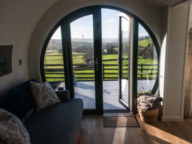 A seating area with a sofa and pillows next to a round glass door opening to a balcony with a view of green fields at Creuddyn in Llanfihangel-y-Creuddyn near Aberystwyth