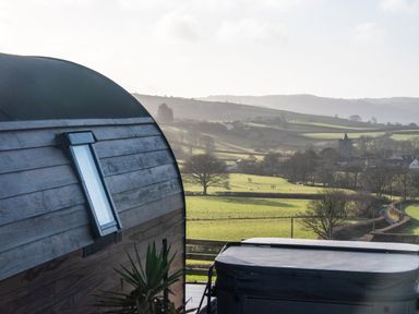A wooden cabin with a window and a covered hot tub overlooking green fields and hills at Creuddyn in Llanfihangel-y-Creuddyn near Aberystwyth