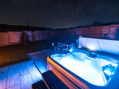 A backyard at night with a lit hot tub a wooden fence and starry sky at Creuddyn in Llanfihangel-y-Creuddyn near Aberystwyth