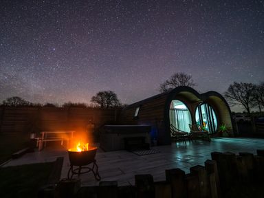 A cabin with curved roof on a patio with chairs and a fire pit under a starry night sky at Creuddyn in Llanfihangel-y-Creuddyn near Aberystwyth