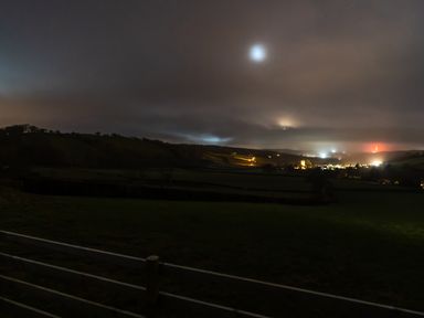 A night landscape with hills and a distant town illuminated by lights and a fence in the foreground at Creuddyn in Llanfihangel-y-Creuddyn near Aberystwyth