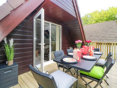 An outdoor dining area with a black table and chairs on a wooden deck at 17 Valley Lodges in Gunnislake