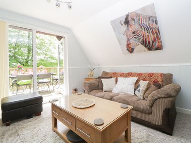 A living room with a brown sofa white pillows wooden coffee table and glass door opening to a balcony at 17 Valley Lodges in Gunnislake