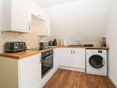 A kitchen with white cabinets wooden countertop a washing machine and appliances at 17 Valley Lodges in Gunnislake