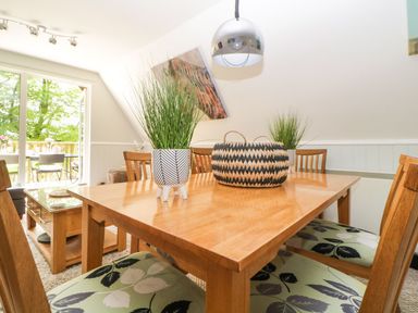 A dining room with a wooden table and chairs with patterned cushions plants on the table and a sliding door leading outside at 17 Valley Lodges in Gunnislake