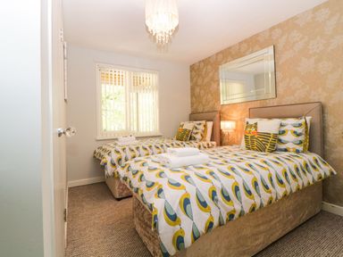 A bedroom with two single beds with bird patterned bedding a window with blinds and a wall mirror at 17 Valley Lodges in Gunnislake