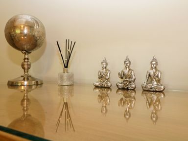 A tabletop with a silver globe, a reed diffuser, and three small seated Buddha statues at 17 Valley Lodges in Gunnislake