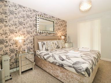 A bedroom with a double bed linens bedside tables with lamps and a large mirror on floral wallpaper at 17 Valley Lodges in Gunnislake