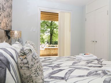 A bedroom with a patterned bedspread pillows a bedside lamp white wardrobe and an open door showing trees outside at 17 Valley Lodges in Gunnislake