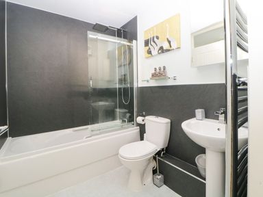 A bathroom with a bathtub and shower, toilet, pedestal sink, and wall art at 17 Valley Lodges in Gunnislake