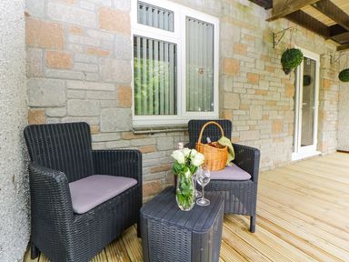 A patio with two black wicker chairs a small table with flowers and wine glasses at 17 Valley Lodges Gunnislake