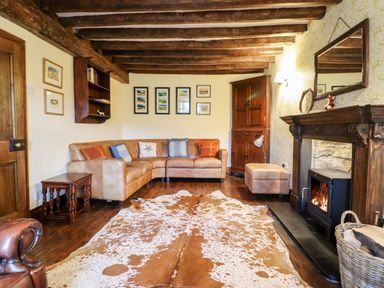 A living room with a leather corner sofa a wooden fireplace a cowhide rug and wooden beams on the ceiling at Gwengraig Brithdir near Dolgellau