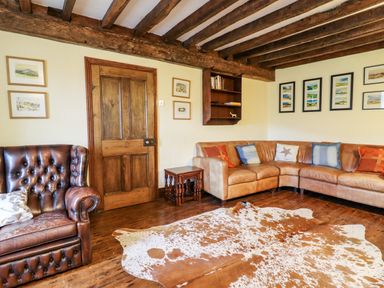 A living room with a brown leather lounge chair a curved leather sofa with cushions a wooden door framed pictures on the walls a small wooden table wooden floor and exposed wooden ceiling beams at Gwengraig in Brithdir near Dolgellau