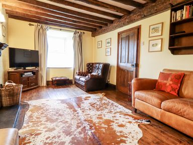 A living room with wooden ceiling beams a leather sofa and armchair a cowhide rug and a television on a wooden cabinet at Gwengraig in Brithdir near Dolgellau