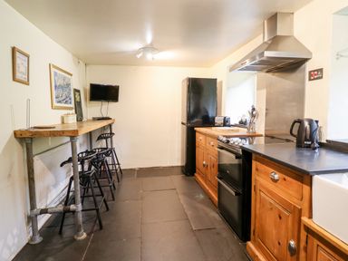 A kitchen with wooden cabinets a black refrigerator a black oven kettle and bar stools at Gwengraig in Brithdir near Dolgellau
