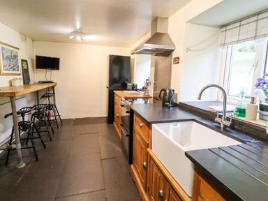 A kitchen with wooden cabinets a black countertop a white sink a black fridge and a breakfast bar with stools at Gwengraig in Brithdir near Dolgellau