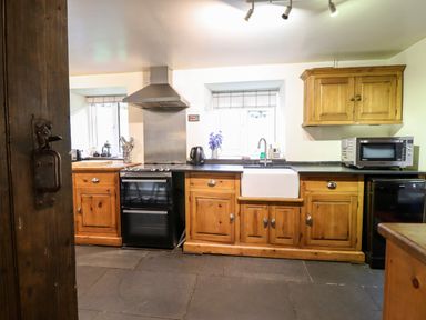 A kitchen with wooden cabinets a stove a white sink a microwave and a kettle at Gwengraig in Brithdir near Dolgellau