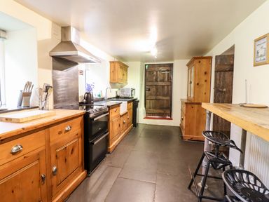 A kitchen with wooden cabinets black stove metal range hood wooden counter a wooden table with two black stools and a wooden door at Gwengraig in Brithdir near Dolgellau