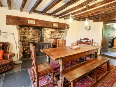 A dining room with a wooden table and chairs near a fireplace with exposed stone at Gwengraig in Brithdir near Dolgellau
