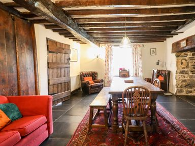 A dining room with wooden table and chairs a red sofa and armchairs with exposed wooden beams at Gwengraig in Brithdir near Dolgellau