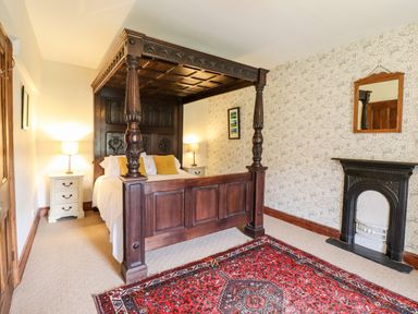 A bedroom with a wooden four-poster bed two bedside tables with lamps a fireplace and a red patterned rug at Gwengraig in Brithdir near Dolgellau