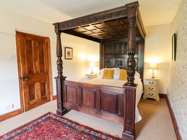 A bedroom with a carved wooden four-poster bed two bedside tables with lamps a wooden door and a red rug on the floor at Gwengraig in Brithdir near Dolgellau