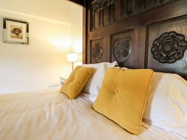 A bed with yellow pillows and a carved dark wood headboard with a lamp and framed flower picture on the wall at Gwengraig in Brithdir near Dolgellau