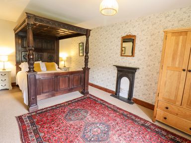 A bedroom with a four poster bed bedside tables lamps a wooden wardrobe a fireplace a mirror and a red patterned rug at Gwengraig in Brithdir near Dolgellau