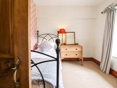 A bedroom with a metal bed a wooden chest of drawers with a lamp and mirror and curtains at Gwengraig Brithdir near Dolgellau
