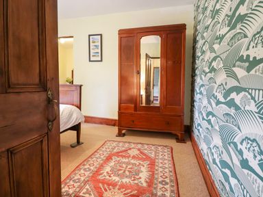 A bedroom with a wooden wardrobe a patterned rug a bed and green and white patterned wallpaper at Gwengraig in Brithdir near Dolgellau