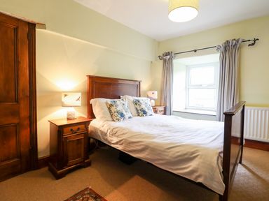 A bedroom with a wooden bed and bedside tables with lamps near window at Gwengraig in Brithdir near Dolgellau