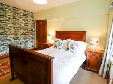 A bedroom with a wooden bed frame floral pillows two wooden bedside tables with lamps and patterned wallpaper at Gwengraig in Brithdir near Dolgellau