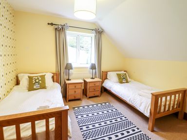 A bedroom with two single beds wooden nightstands and a window at Gwengraig in Brithdir near Dolgellau