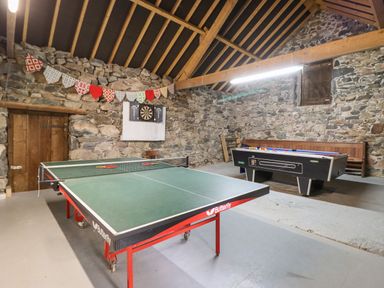 A game room with a ping pong table pool table and dartboard on a stone wall at Gwengraig in Brithdir near Dolgellau
