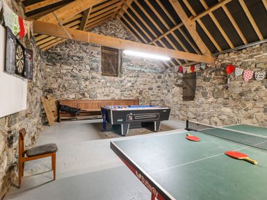 A game room with a ping pong table with paddles a foosball table a bench a chair and a dartboard on a stone wall at Gwengraig in Brithdir near Dolgellau