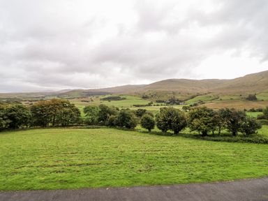 A green field with trees and rolling hills under a cloudy sky at Gwengraig in Brithdir near Dolgellau