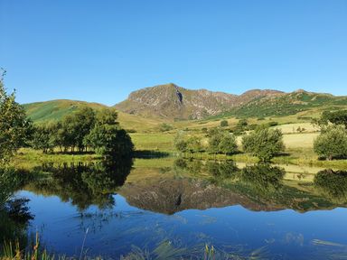 A lake reflecting trees and hills under a clear sky at Gwengraig in Brithdir near Dolgellau